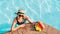 Soulful smiling woman in straw hat in sunglasses swimming in pool and enjoying fresh tropical fruits