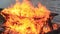Sound. Close-up video of a burning picnic table with increasing intensity by a body of water.