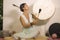 Sound healing and meditation therapy - attractive and elegant Asian Chinese healer woman playing drum at yoga studio as relaxation