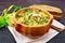 Soup with couscous and spinach in clay bowl on wooden table