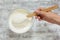 Sour cream in white bowl with wooden spoon in woman hand on white background