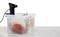 Sous vide cooker and vacuum packed food products in box on wooden table against white background, space for text. Thermal