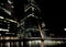 The South Quay Footbridge At South Dock In Front Of The Brightly Lit Bank Towers Of Canary Wharf London England At Night