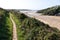 The South West Coast Path runs beside the river Gannel with people enjoying the sandy beach in the sun on a hot late summer day