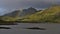 Southeastern coast of VestvÃ¥gÃ¸y island, Lofoten, Norway with rocks in water, rugged mountains and strong rainbow.