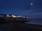 Southwold Pier lit up at night next to a wooden groyne under a bright moon with a ship on the horizon, Suffolk