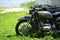 The Soviet Dnepr motorcycle on the green grass of the front part close up against a sandy shore by the lake