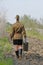 Soviet female soldier in uniform of World War II with suitcase goes on a plowed road