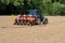 Sowing seeds machine trailed by tractor on a plowed field in springtime.