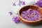 Spa and wellness composition with perfumed lilac flowers water in wooden bowl and terry towel on stone background, aromatherapy