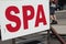 spa writing caption text sign signboard with road behind with person walking. ph