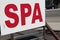 spa writing caption text sign signboard with road behind, red on white. p