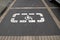 Space marked with white disabled parking symbol painted in white and delimited by light beige tile on gray sidewalk parking lot