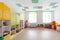 Spacious white game room in the kindergarten with toys, two large windows and tables for classes.