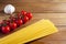 Spaghetti, cherry tomatoes and garlic on a brown wooden table. Tomatoes and garlic to the left of spaghetti.