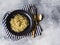 Spaghetti with green sauce in a black bowl, gold appliances on a gray background. Top view. Copy space
