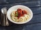 Spaghetti and meatballs in tomato sauce in a ceramic saucer on dark wooden background.