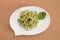 Spaghetti pasta with pesto sauce in white dish in shape of a chat bubble, on cork background.