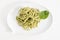 Spaghetti pasta with pesto sauce in white dish in shape of a chat bubble, on white background.