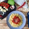 Spaghetti with red sweet pepper and sesame sauce lie on a blue plate on a wooden table