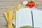 Spaghetti and scattered pasta with notebook and vegetables on a wooden table