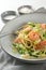 Spaghetti , shrimps, zucchini and spring onions, a healthy Mediterranean meal  in a grey plate with a fork, napkin and spice bowls