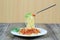 Spaghetti with tomato sauce on silver fork of floating in the white dish on wooden floor.