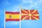 Spain and North Macedonia two flags on flagpoles and blue cloudy sky