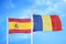Spain and Romania two flags on flagpoles and blue cloudy sky