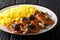 Spanish Catalan beef fricando with gravy and wild mushrooms served with spicy yellow rice and herbs close-up a black table.