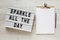 `Sparkle all the day` words on a lightbox, clipboard with blank sheet of paper on a white wooden surface, top view. Overhead, fr