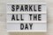 `Sparkle all the day` words on a lightbox on a white wooden surface, top view. Overhead, from above, flat lay. Close-up