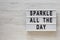 `Sparkle all the day` words on a modern board on a white wooden background, top view. Overhead, from above, flat lay. Space for