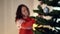 Sparkling ball on New Year tree with blurred Caucasian slim young woman hanging decoration at background leaving