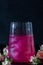 A sparkling brilliant raspberry drink in a glass stands on a wooden table with ice. In the background are roses and a garland