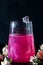 A sparkling brilliant raspberry drink in a glass stands on a wooden table with ice. In the background are roses and a garland