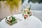 Sparkling wedding glasses with champagne, orchid flower decor and wedding rings in box in blur on white table outdoors, copy space