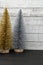 Sparkly gold and silver bottle brush Christmas trees against a white wood background