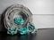 Sparkly gray nest wrapped up with teal blue paper rose flower blooms on a black slate and shiplap background