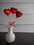 Sparkly red hearts on sticks with a red bow in a white glass vase against a black slate and gray shiplap background, perfect for