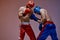 Sparring of two fighting males in helmets and boxing gloves with fit bare torsos during battle, martial arts