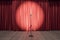 Speaker performance concept with round spotlight on red curtain and microphone on wooden floor of empty stage