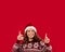Special Christmas offer. Millennial woman in winter holiday outfit pointing upwards at blank space on red background
