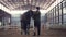 in special hangar, a disabled man jockey strokes a muzzle of a thoroughbred, black horse. man has prosthesis instead of