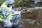 Specialist in a protective suit and mask, on the pond, calls the mobile phone management, to report the results of the study,