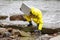 Specialist in protective suit taking sample of water to container on rocky shore