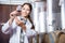 Specialist in white coat examines glass of wine on the background of barrels for fermentation