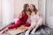 Spectacular girl in red night-suit sharing rumors with best friend and eating pizza. Joyful female models in pyjamas