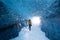 Spectacular natural landscapes inside a blue ice cave, with a woman in yellow looking outside the cave in Iceland