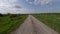 Speed aerial view flight over dirt road surrounded by lush greenery grass plant approaching highway